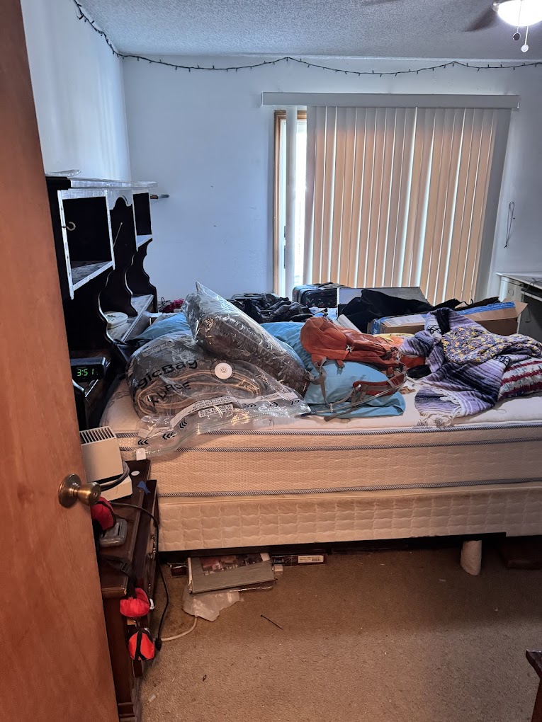 Bedroom with a bunch of junk piled on the bare mattress